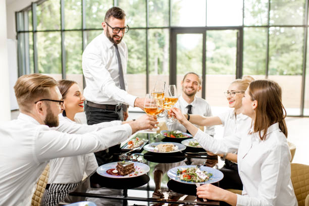 Group of business people dressed in white shirts clinking with wine glasses during a business lunch with delicious meals at the modern restaurant